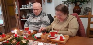 Manželský pár - členové SONS sedí u vánočně vyzdobeného stolu s kávou a dezertem